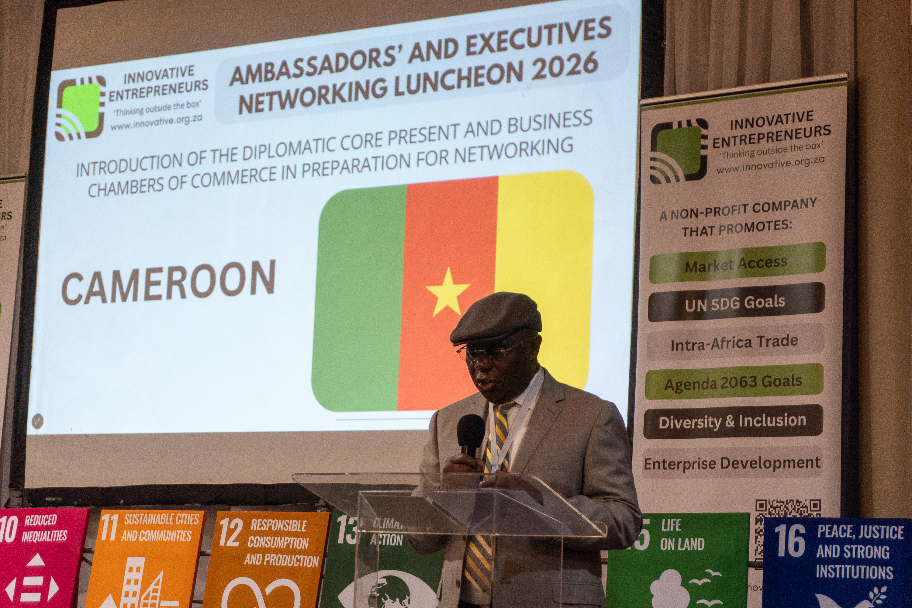 A Cameroon diplomatic representative speaks at AENL 2026 with the Cameroon flag projected behind