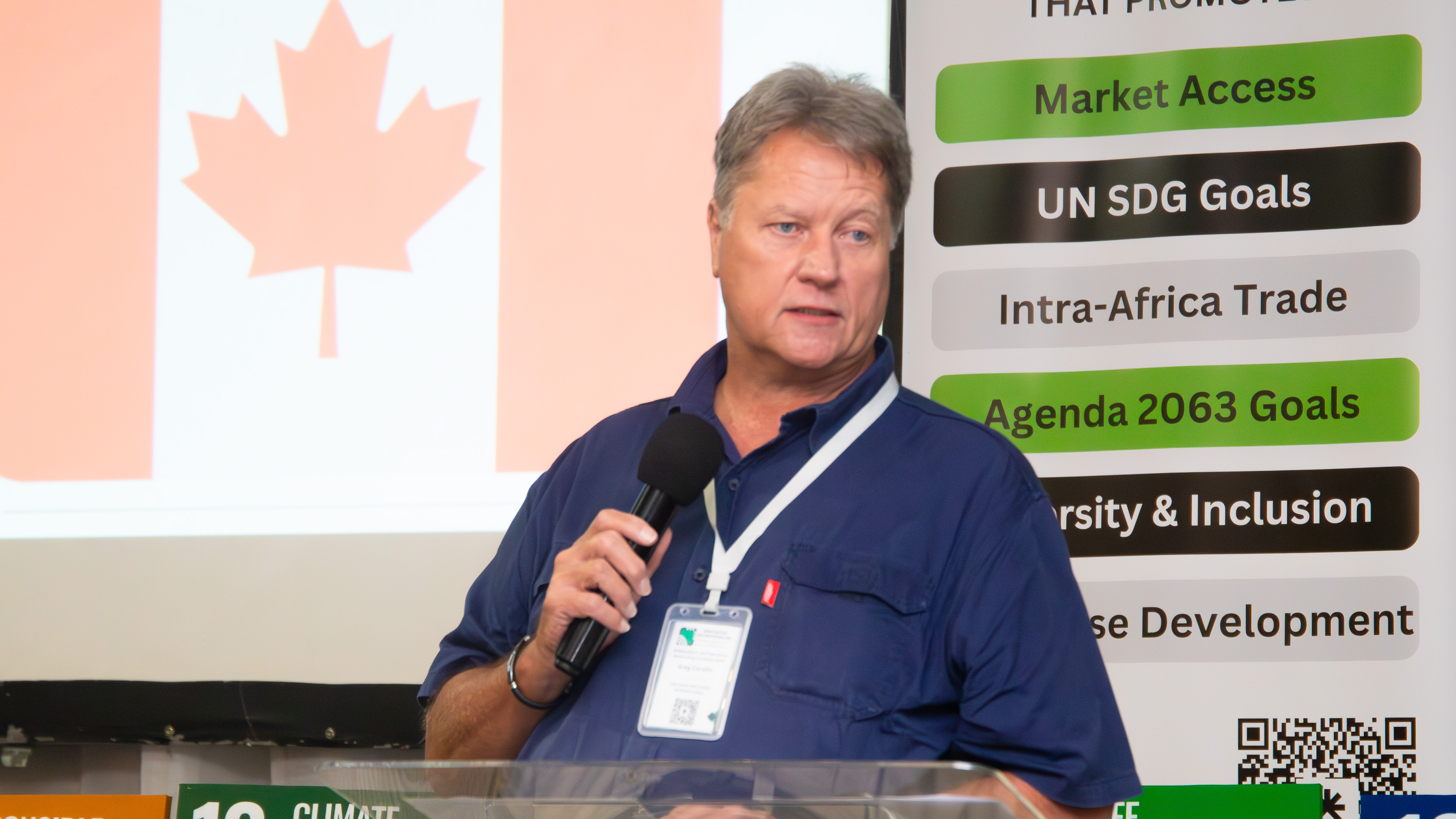 A Canadian diplomatic representative addresses AENL 2026 with the Canada flag projected behind