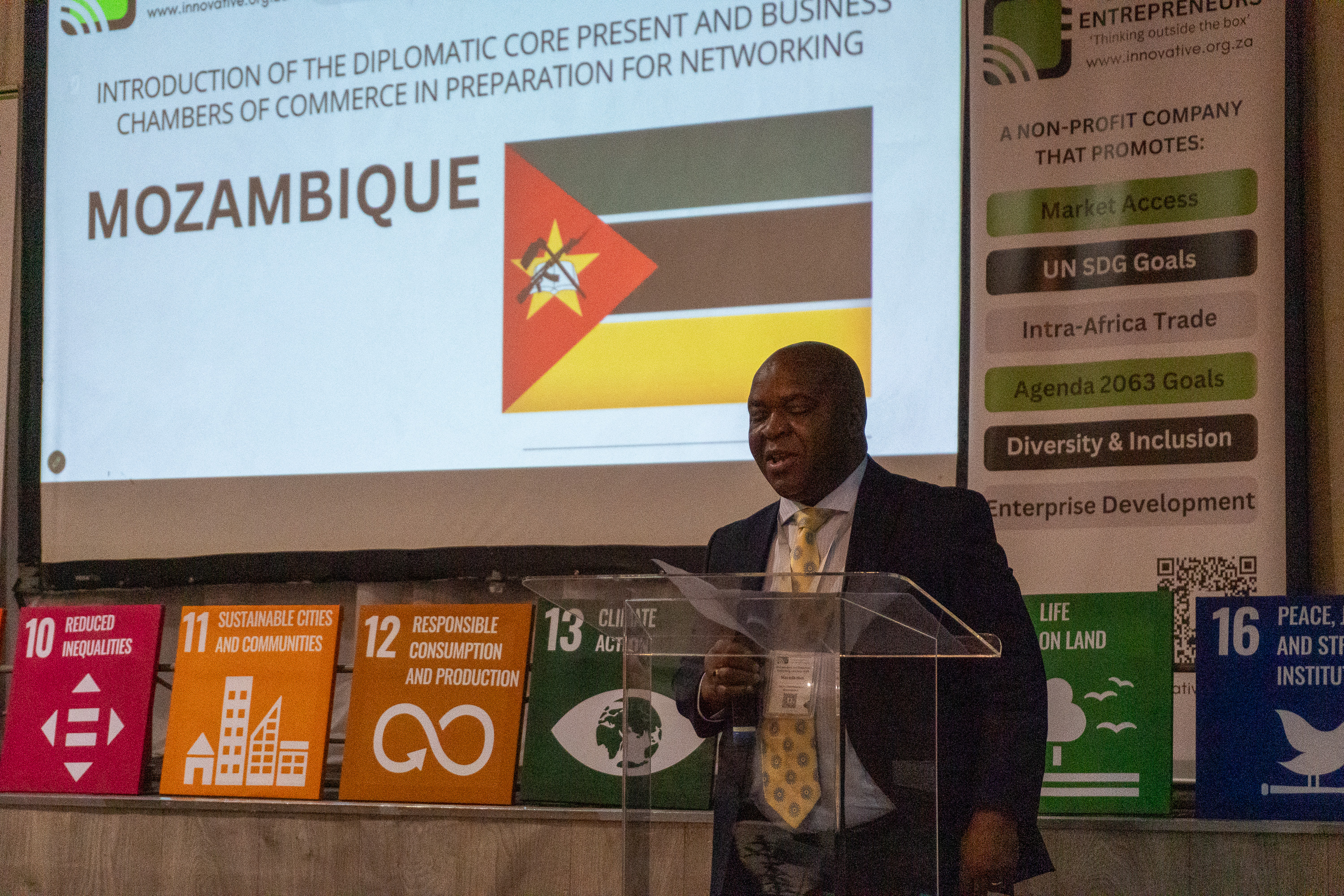 A Mozambican diplomatic representative addresses AENL 2026 with the Mozambique flag projected behind