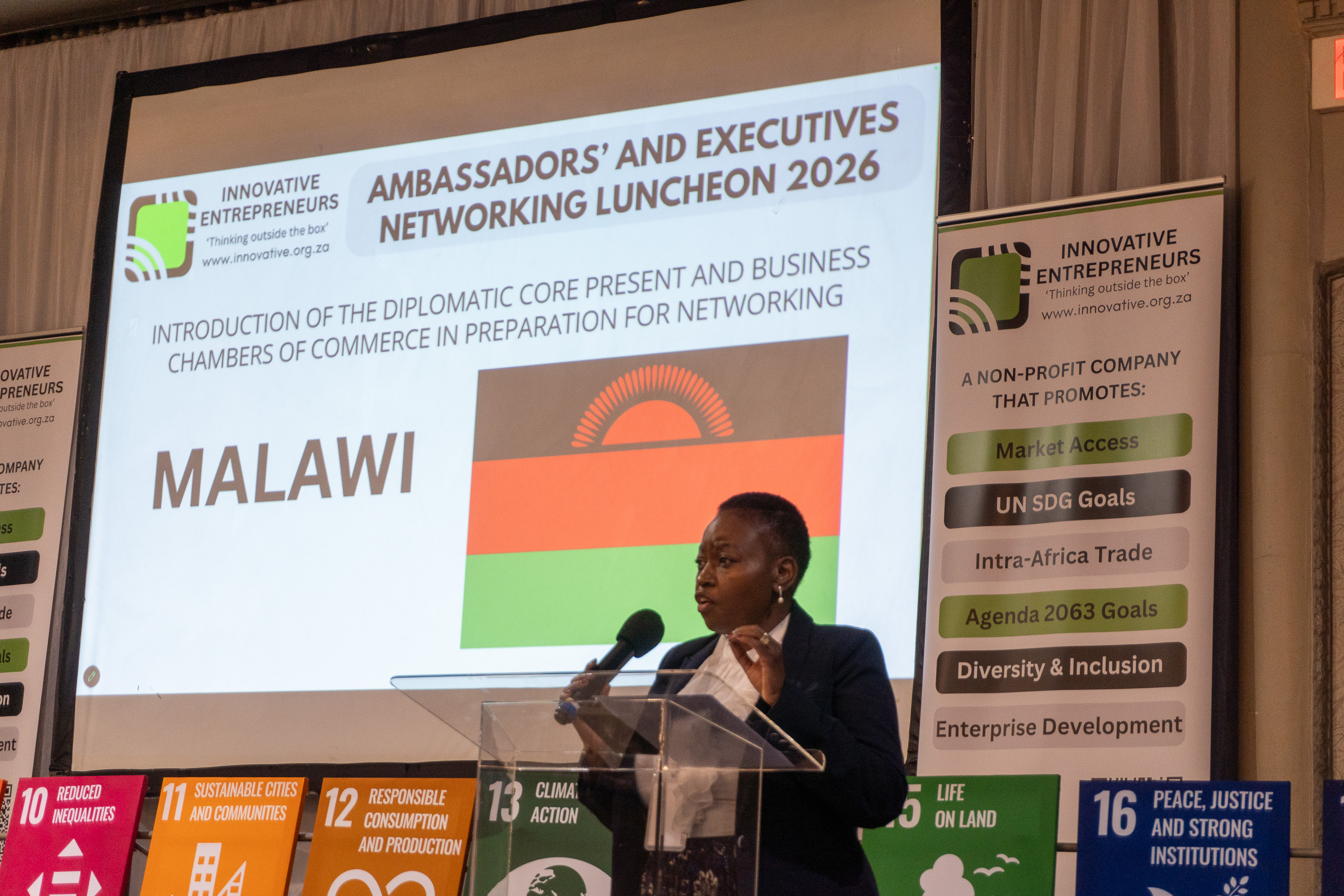 A Malawian diplomatic representative speaks at AENL 2026 with the Malawi flag projected behind