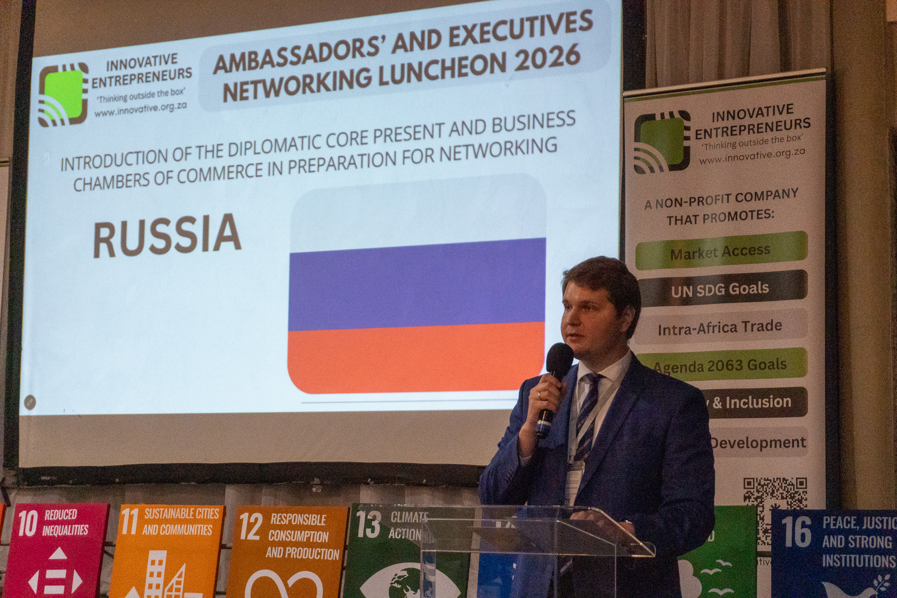 A Russian diplomatic representative addresses AENL 2026 with the Russia flag projected behind